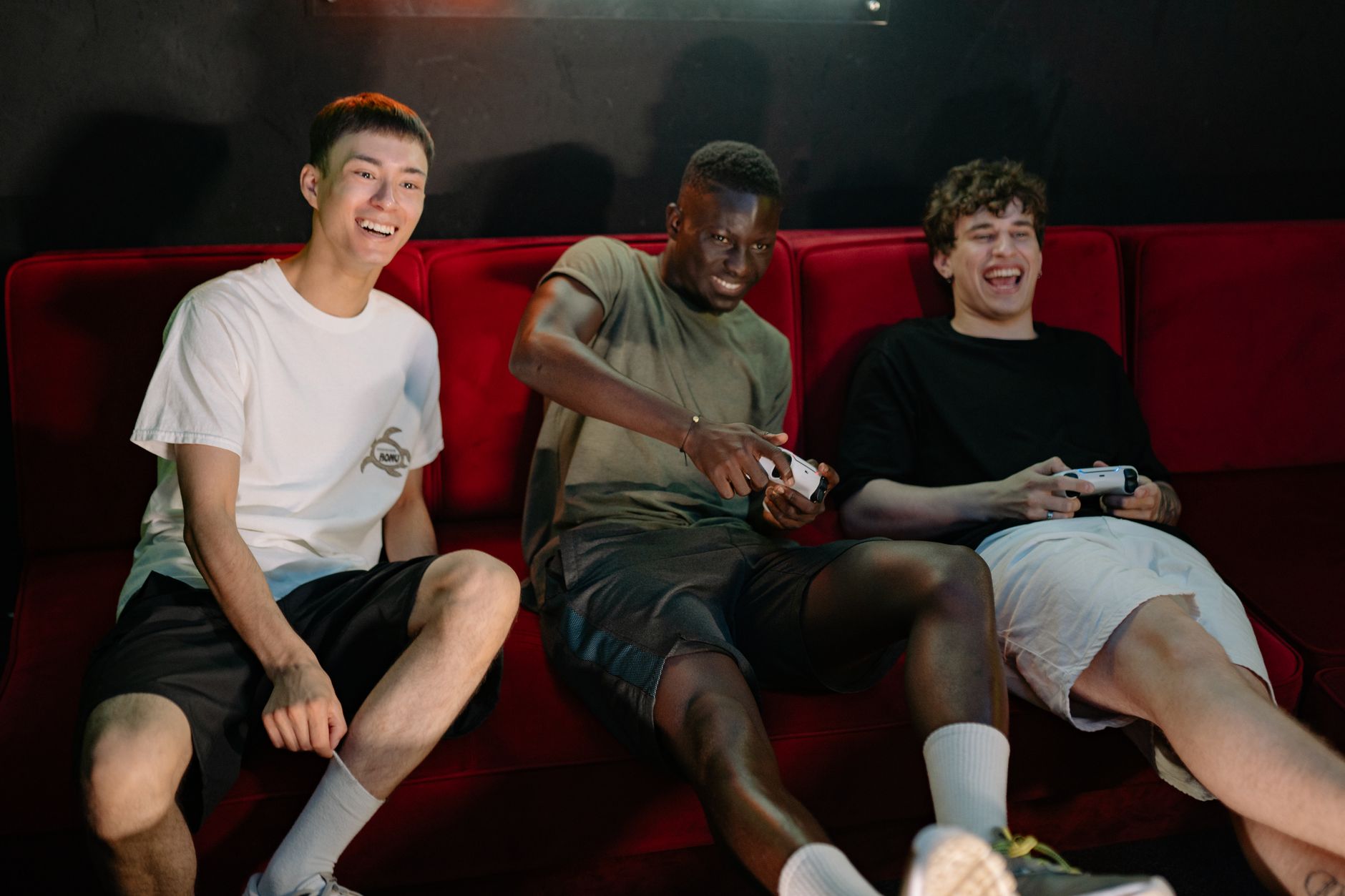 Three diverse young men sitting on a red couch, enjoying a fun video game session together. — 9 Interesting Facts About Onlin