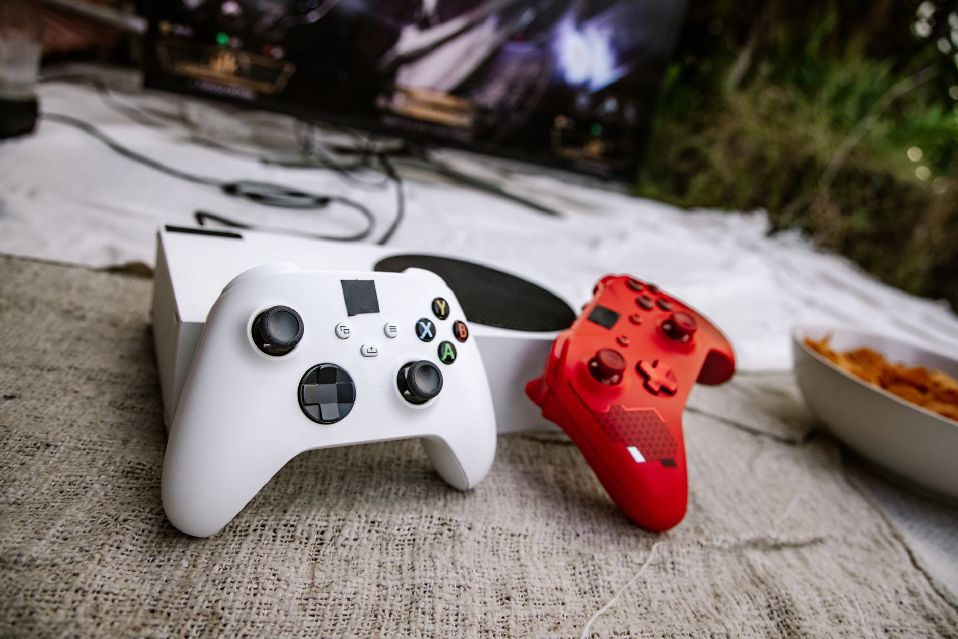 White and red wireless gaming controllers on a textured surface near chips and a TV screen. — Avoid Making These Mistakes Whe