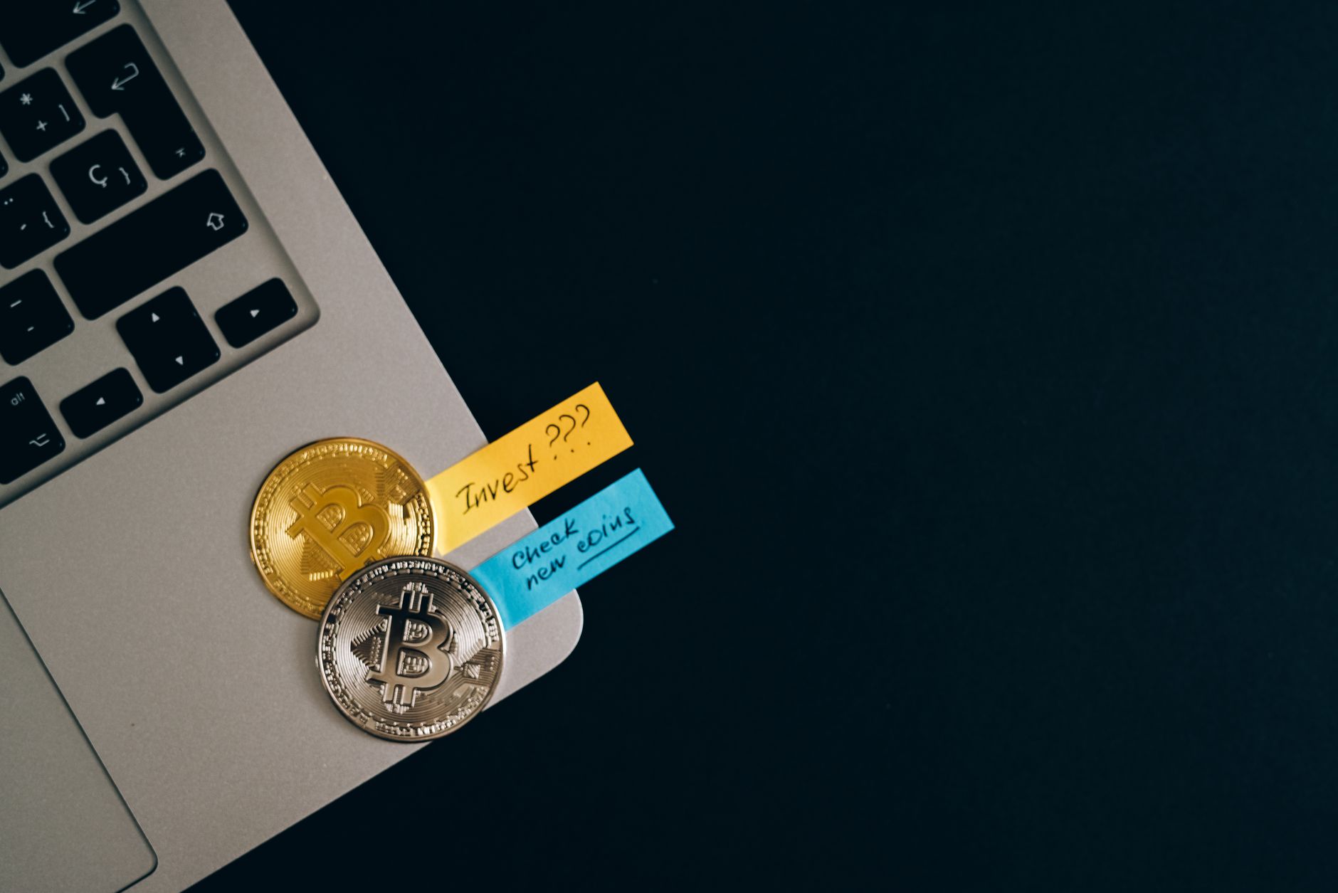 Bitcoin coins placed on a laptop keyboard with sticky note reminders about investing and checking new coins. — BitGo Prime: A