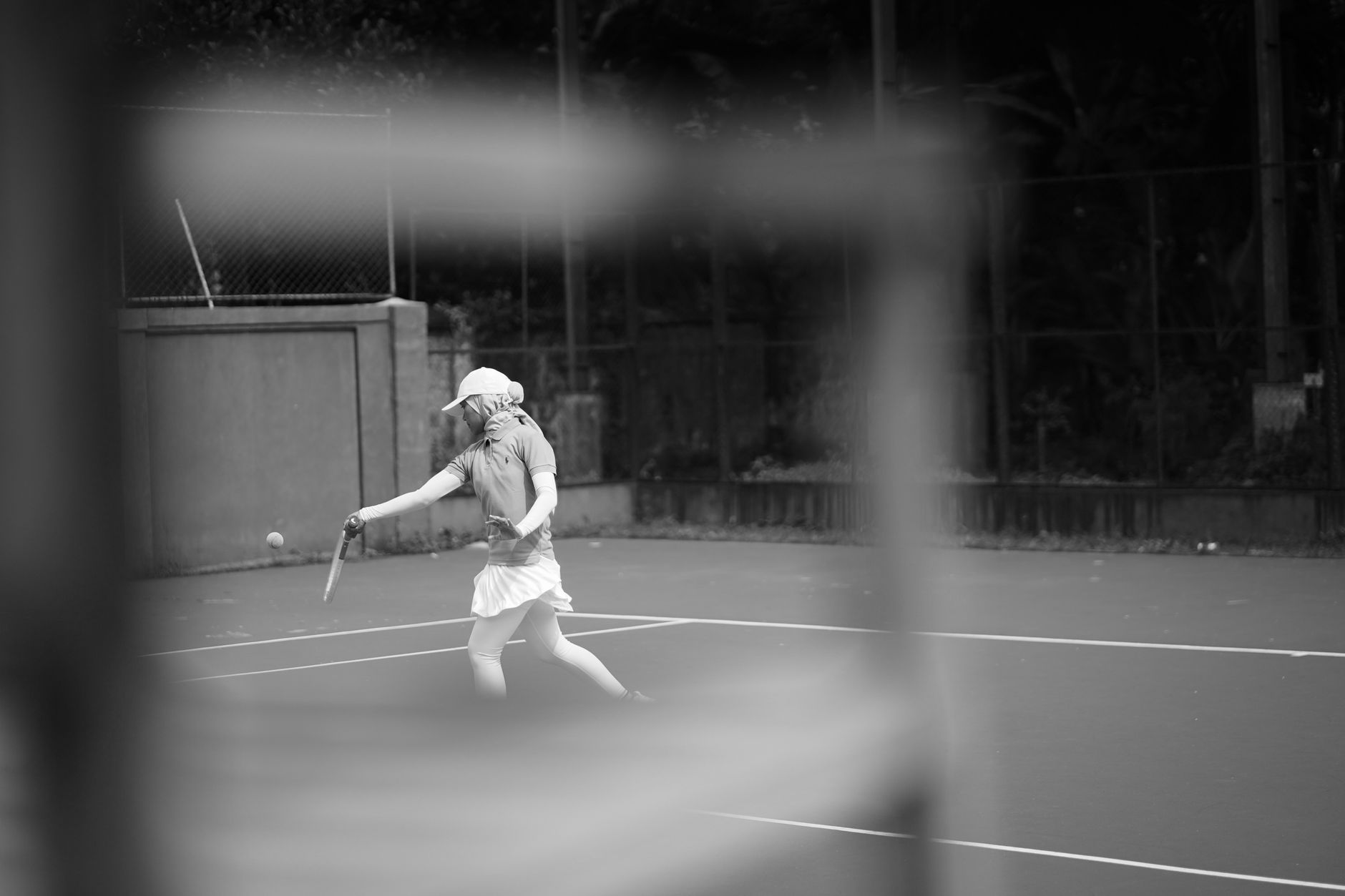 A dramatic black and white photo capturing a tennis player mid-swing on an outdoor court. — Choosing effective and right foot