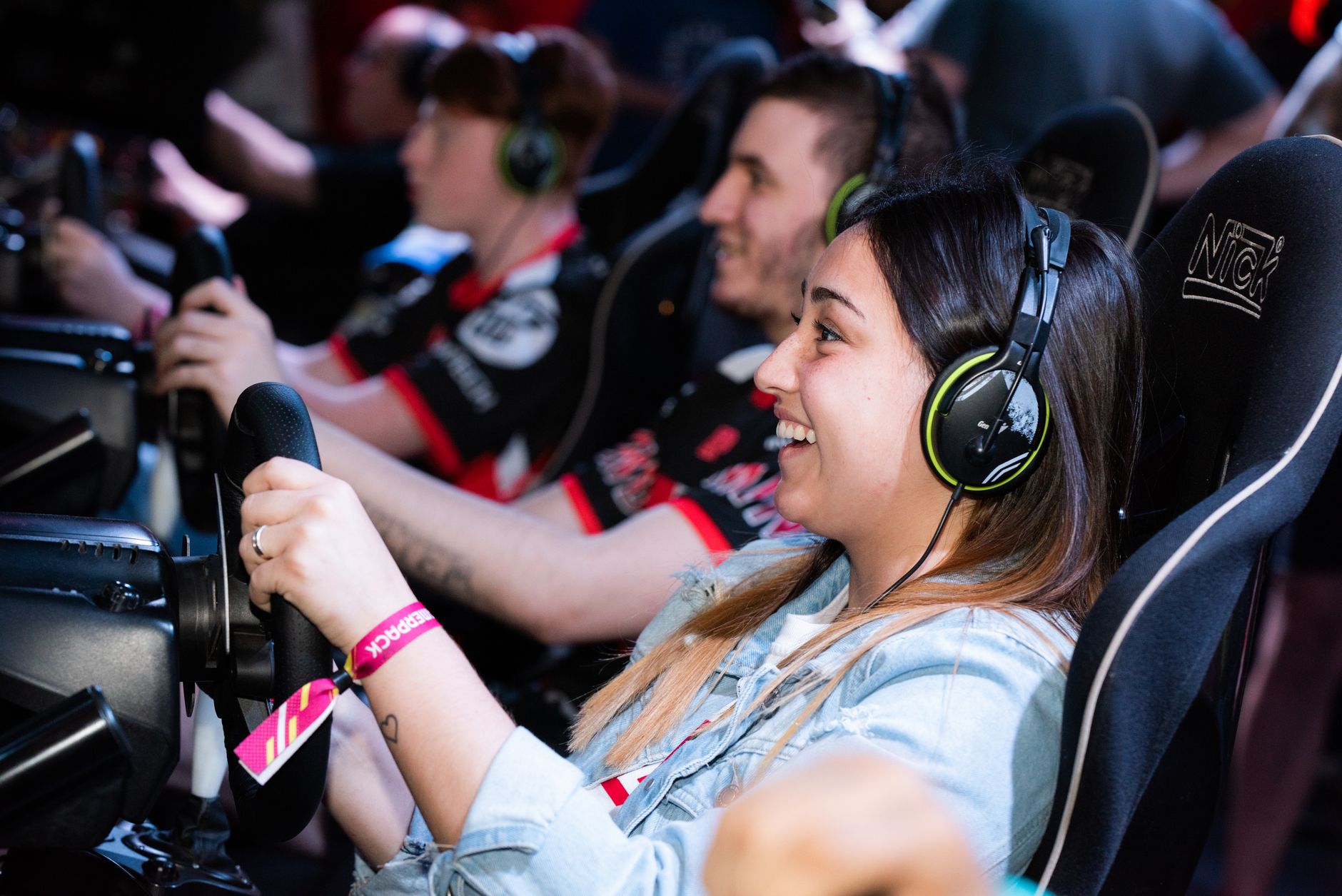 A group of people enjoying an immersive gaming experience at an e-sports center with headphones and steering wheels. — Could