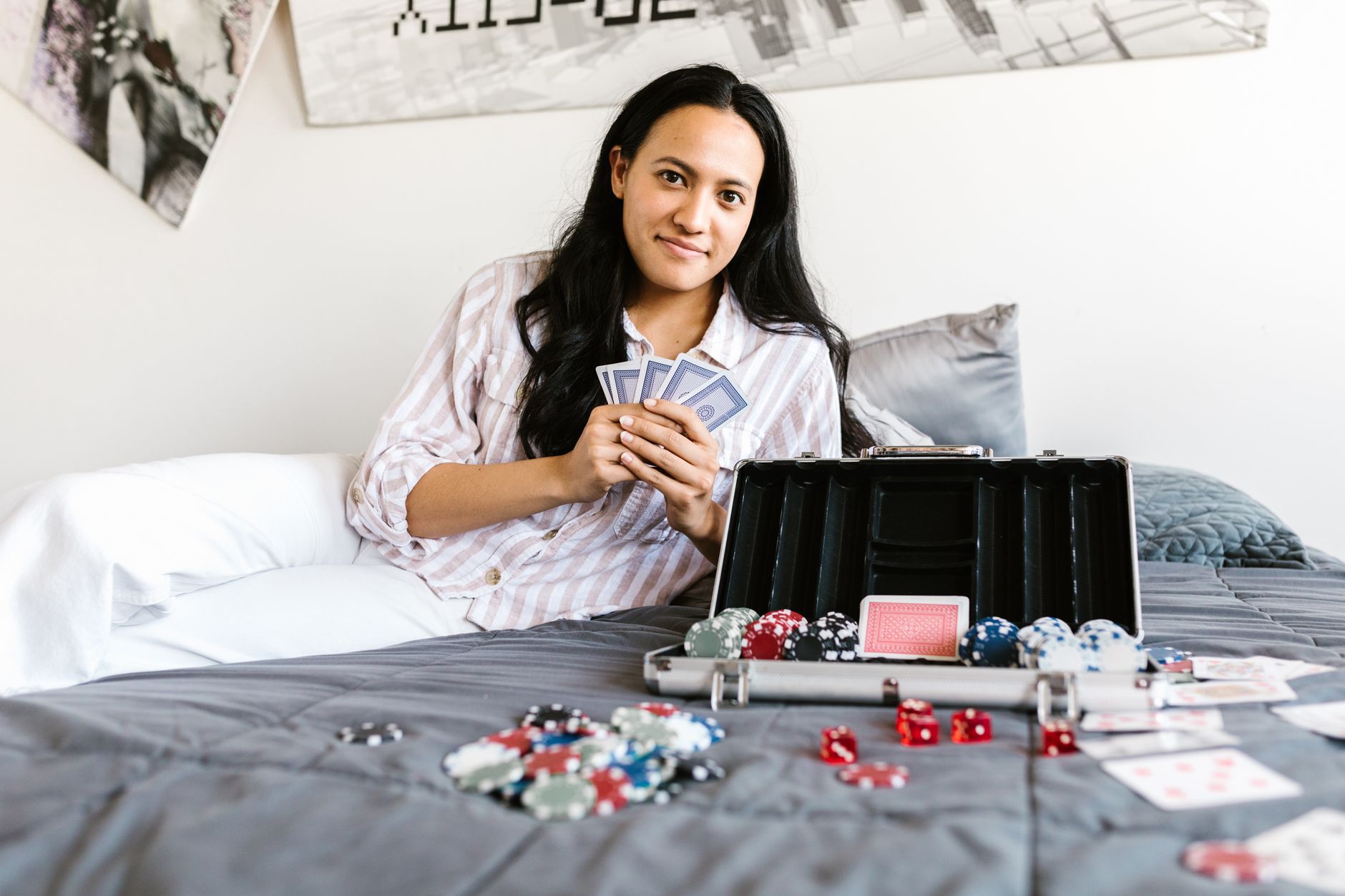 A young woman enjoys a game of poker on her bed, surrounded by cards and chips, creating a casual and playful atmosphere. — K