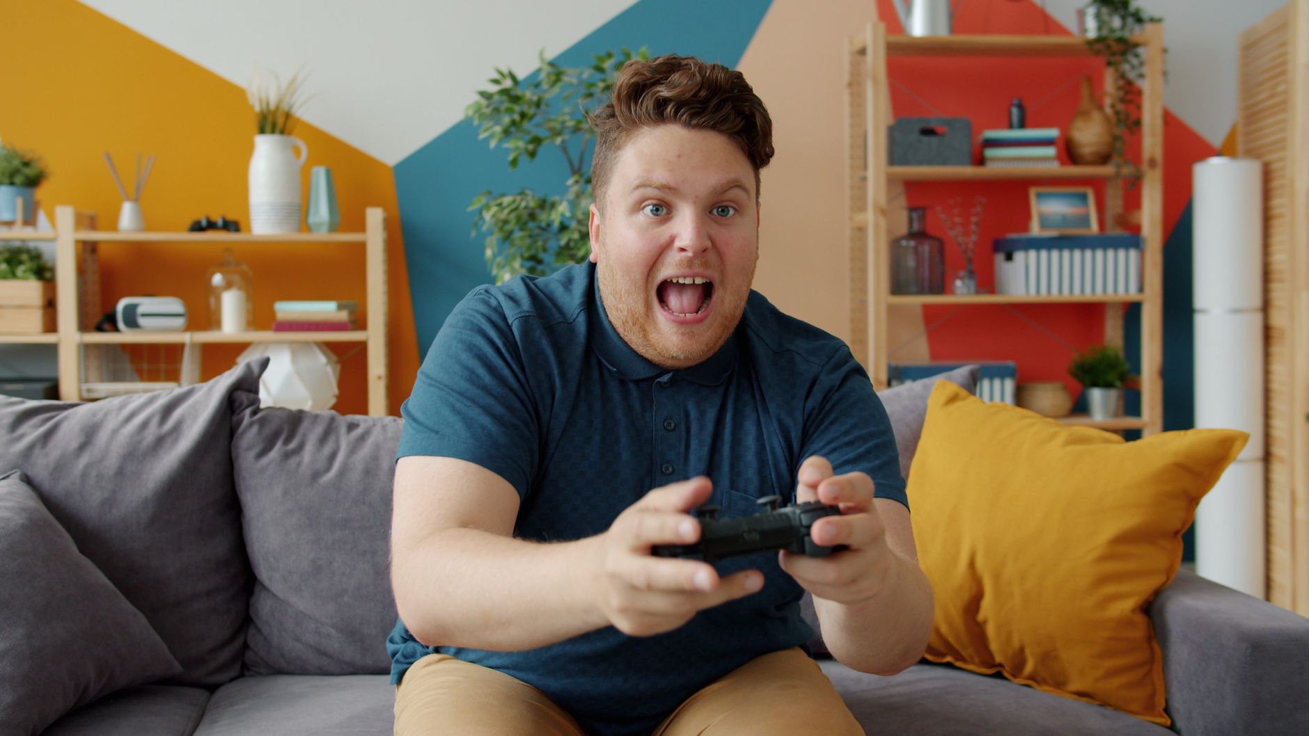 Enthusiastic adult male playing video game on console in colorful, modern living room. — Methods for correct playing in on-li