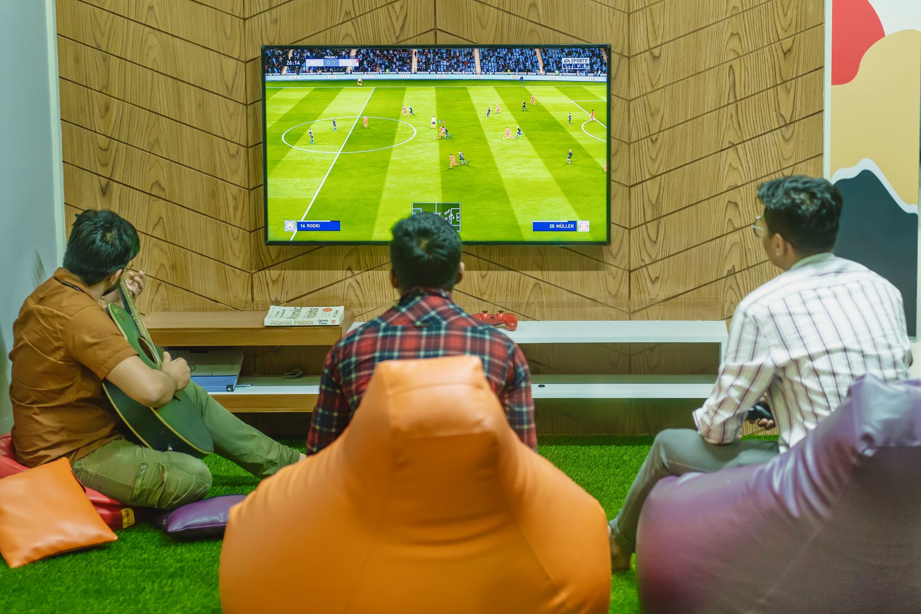 Three friends relaxing and playing a soccer video game indoors on a comfortable game night. — Read Our TrustPilot Review for