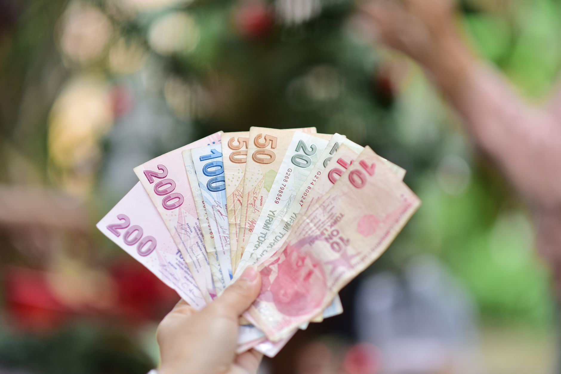 A hand holding multiple Turkish Lira banknotes in an outdoor setting, showcasing various denominations. — The Top Seven Onlin