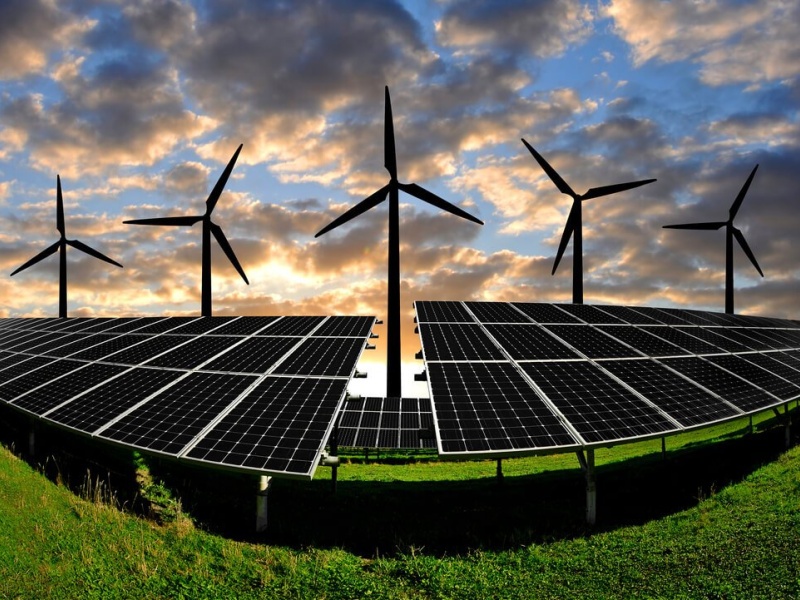 Wind turbines and solar panels in a landscape during sunset